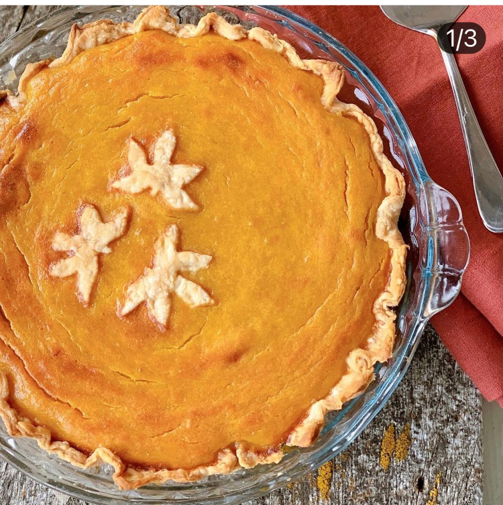 Pumpkin pie with leaf decorations on a rustic table.