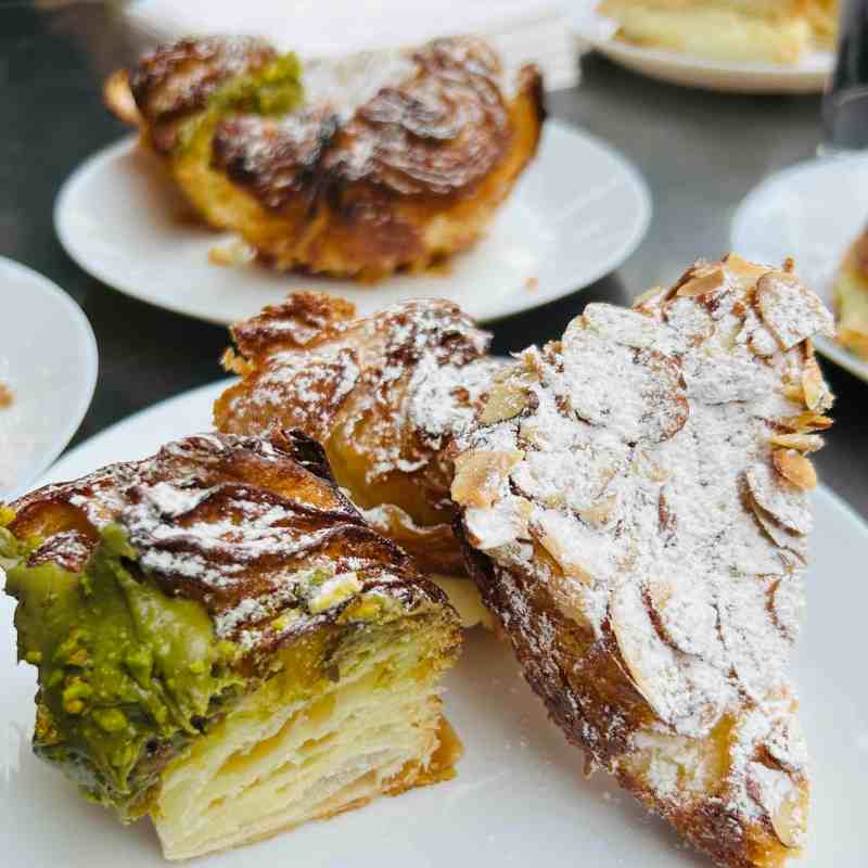 Close-up of pastries on white plates, topped with powdered sugar and almonds.