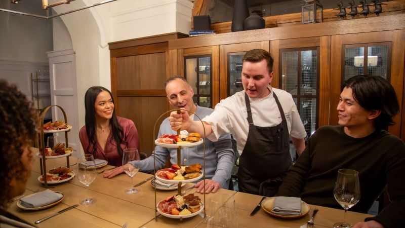 Chef serving guests at a dining table with tiered platters of food.