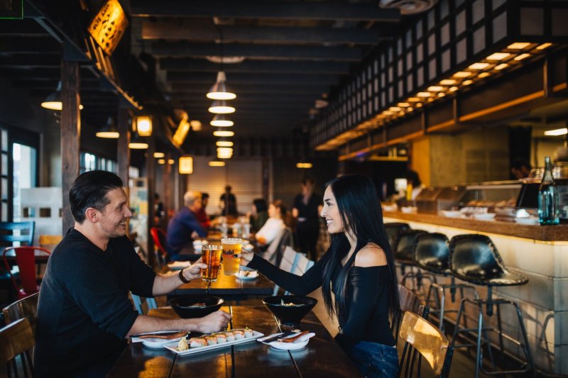 Man and woman toasting with beer in a restaurant with sushi on table.