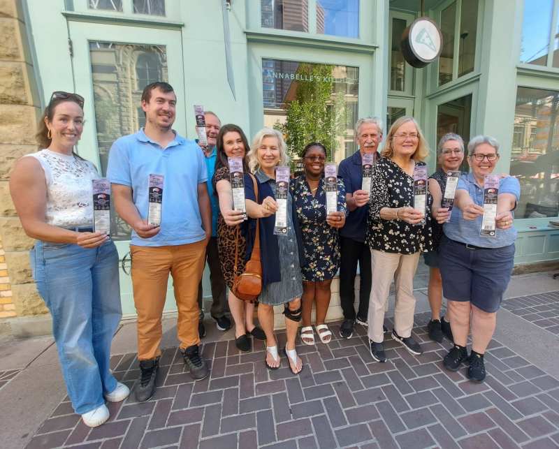 Group of people smiling and holding event flyers outside a building.