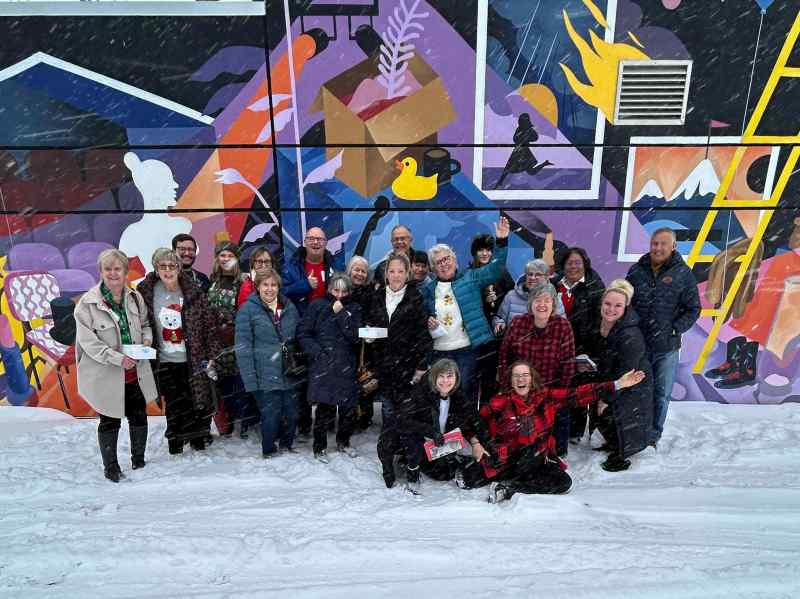 Group of people posing in front of a colorful mural on a snowy day.