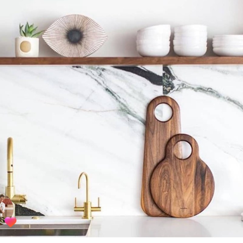 White kitchen with marble backsplash, wood cutting boards, and gold faucet.