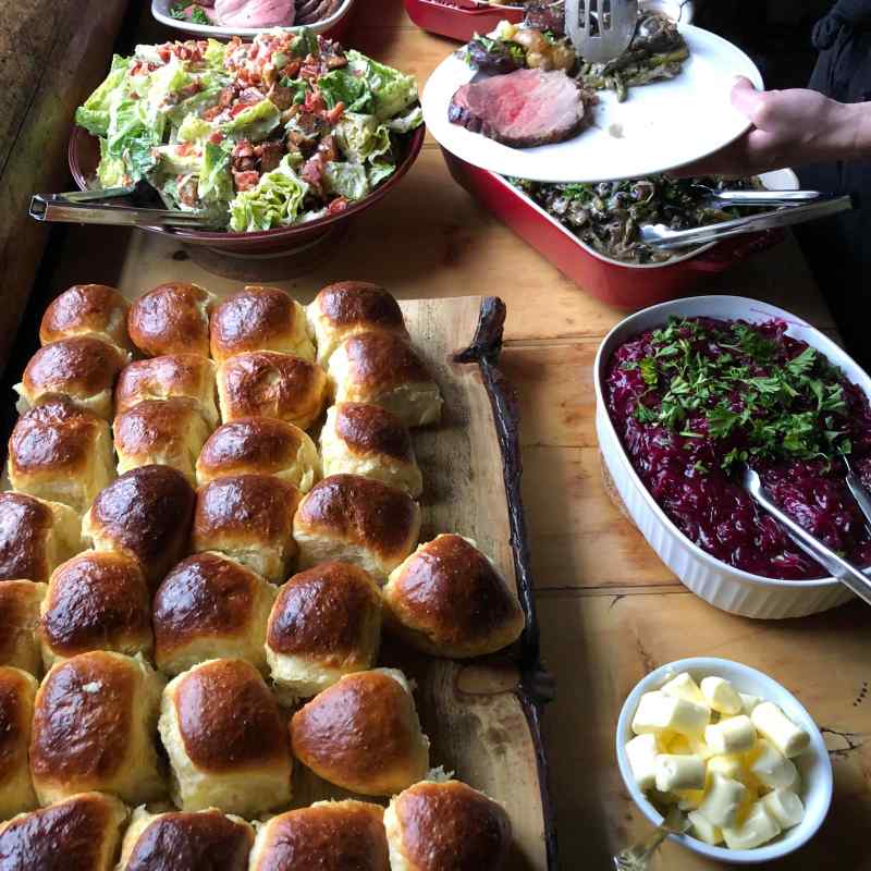 Buffet with rolls, salad, roast beef, potatoes, red cabbage, and butter on a wooden table.