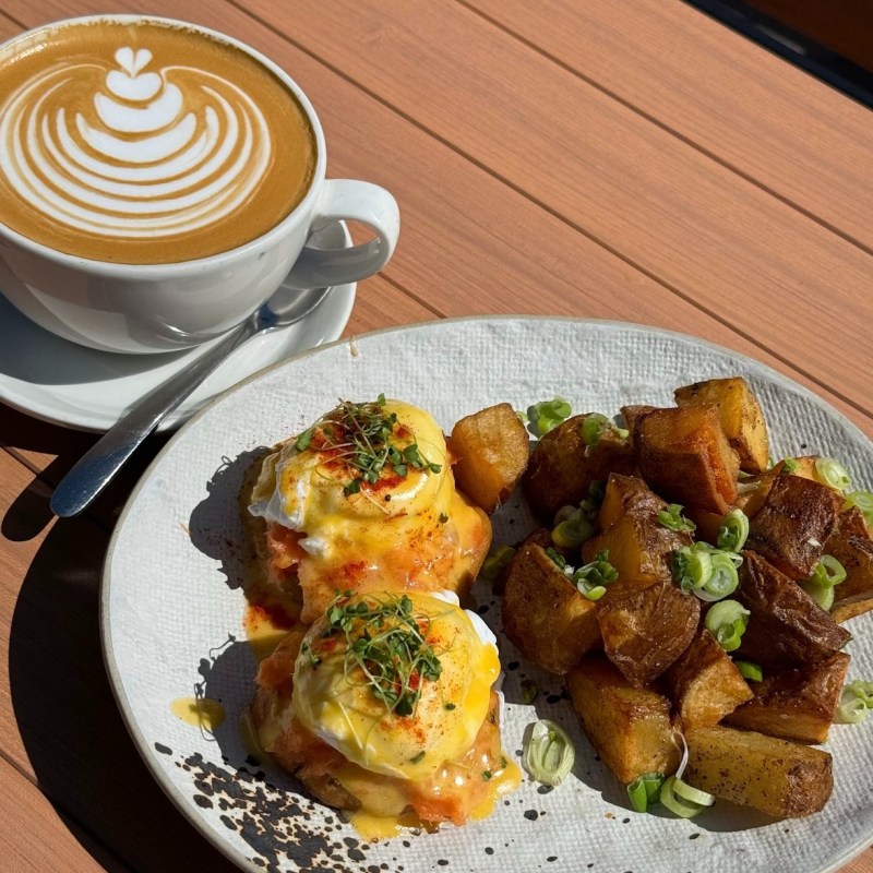 Coffee with latte art and Eggs Benedict with potatoes on a plate.