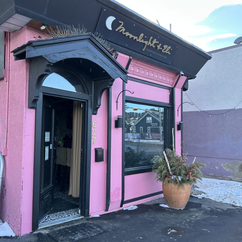 Pink storefront with black trim, a large window, and a potted plant outside.
