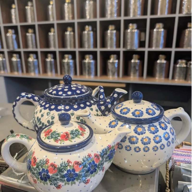 Three decorative teapots with floral patterns in front of tea canisters on shelves.