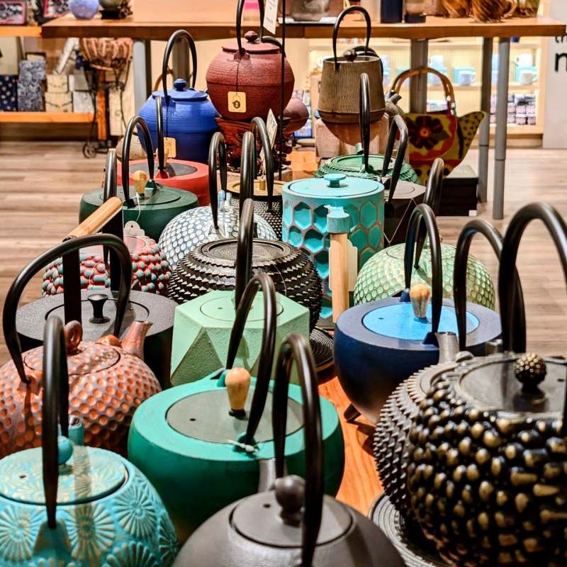 Assorted colorful teapots displayed on a wooden table in a shop.