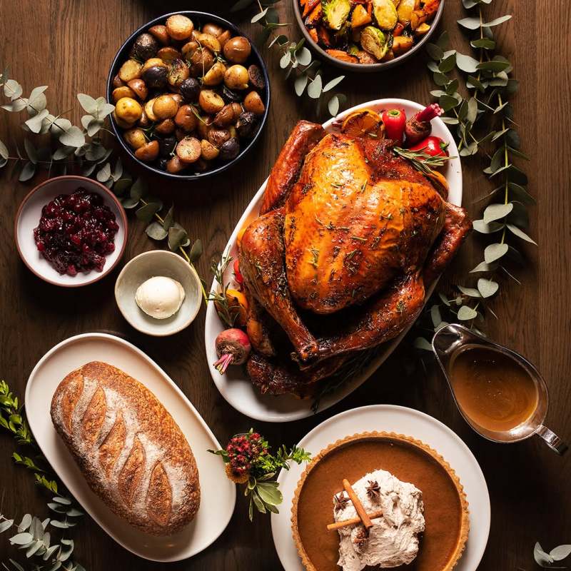 Thanksgiving dinner spread with roasted turkey, vegetables, pie, bread, and various side dishes on a wooden table.