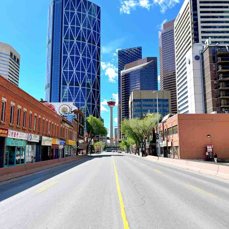 View of an empty city street with tall buildings and a tower in the background.