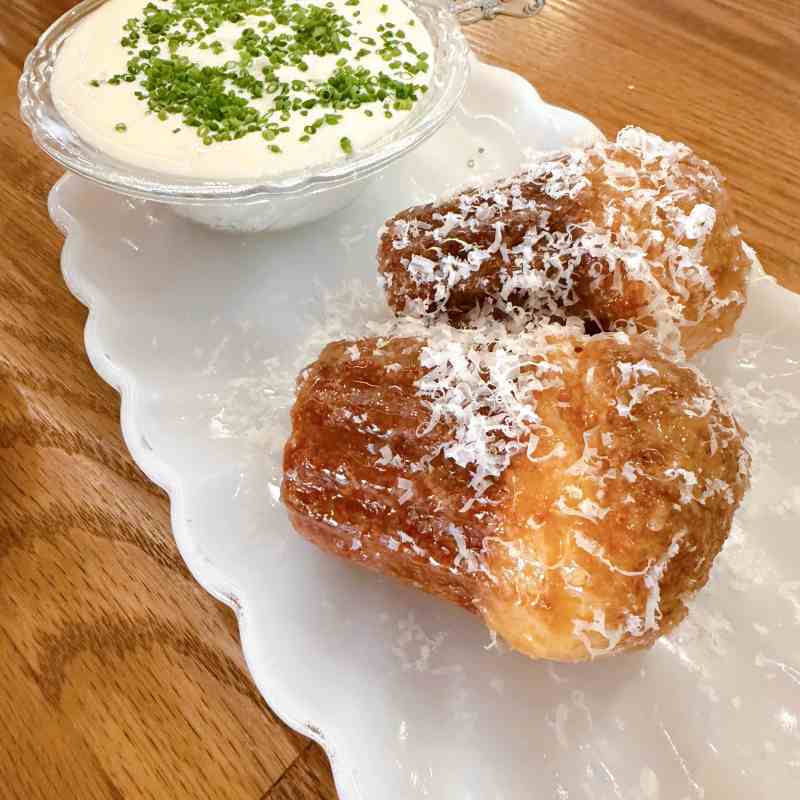 Two pastries with cheese near creamy dip topped with green herbs on a white plate.