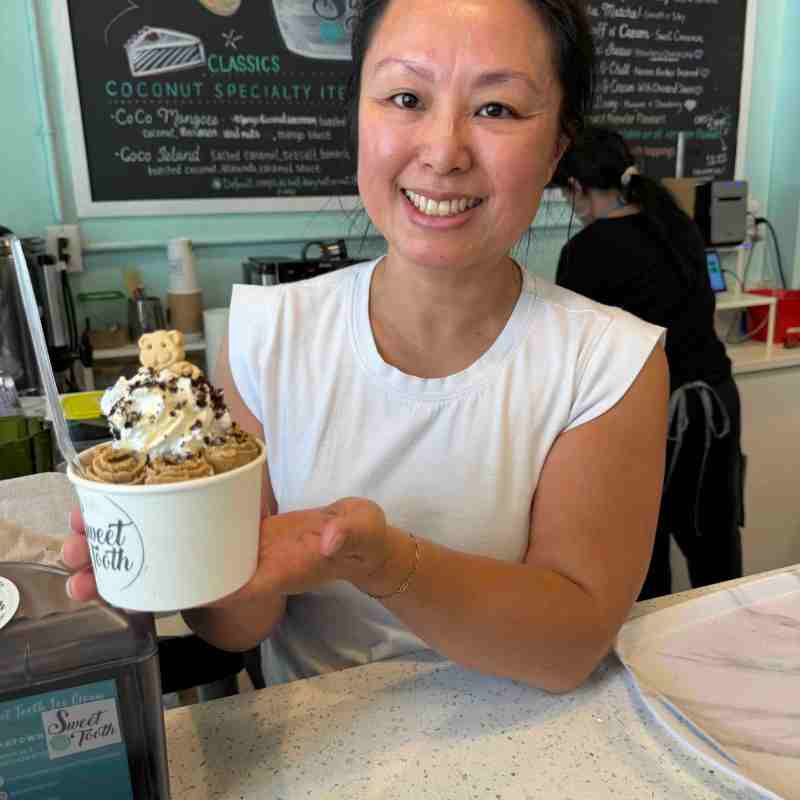 Smiling woman holds ice cream cup with toppings in a shop.