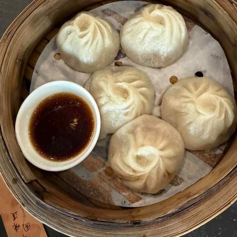 Steamed dumplings in a bamboo basket with a small dish of sauce.