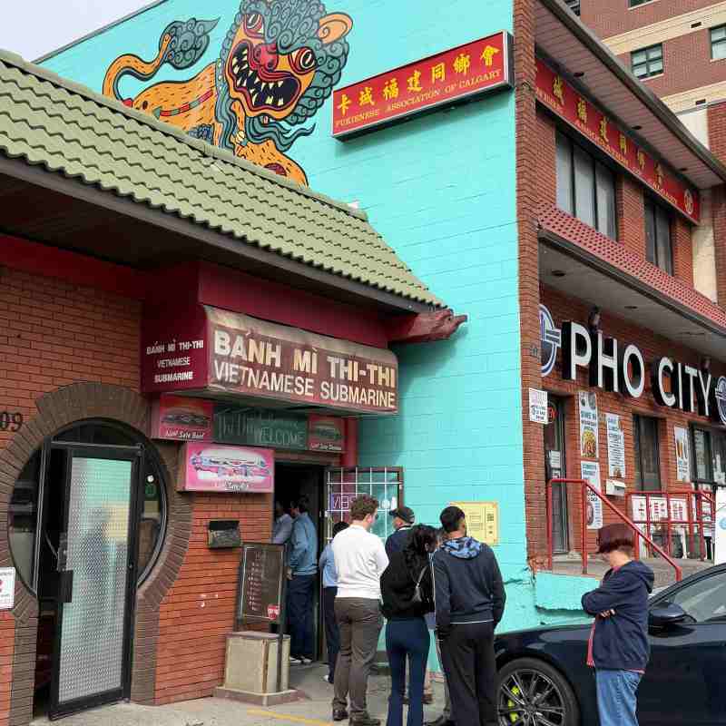 People lined up outside a Vietnamese restaurant with colorful mural.